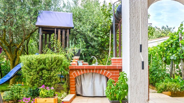 A patio area with a brick fireplace, a wooden bench, and a planter with green plants. - House Bruno (Pula)