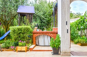 A patio area with a brick fireplace, a wooden bench, and a planter with green plants. - House Bruno (Pula)