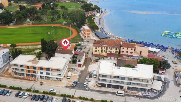 A coastal town with a beach, a sports field, and several buildings including a hotel with a red roof. - Apartment Vladimir (Medulin)