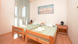 Una camera da letto con due letti di legno, un quadro con dei velieri e una finestra con tende leggere.