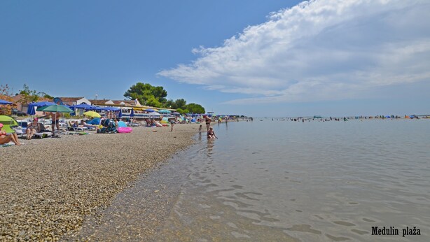 Una spiaggia con ciottoli, ombrelloni e persone.