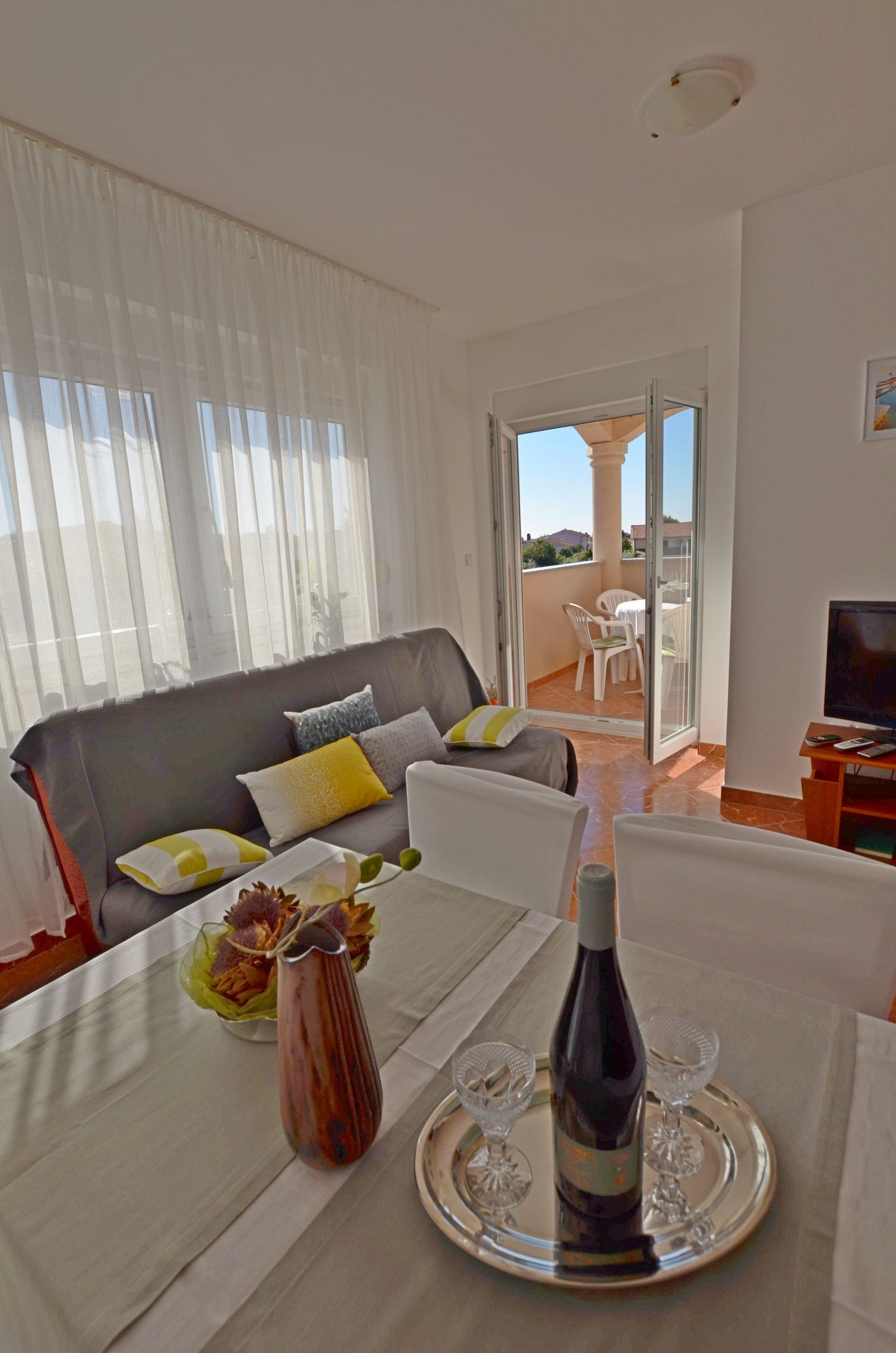 Ein Wohnzimmer mit einer Couch, einem Esstisch mit Flasche und Gläsern sowie einem Balkon mit Stühlen.