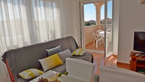 Un soggiorno con divano, un tavolo da pranzo con una bottiglia e dei bicchieri, e un balcone con sedie.