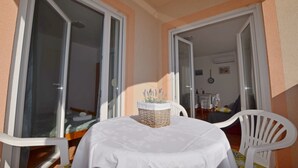 Un balcone con tavolo e sedie, un cesto di vimini con lavanda e uno scorcio dell'interno attraverso una porta aperta.