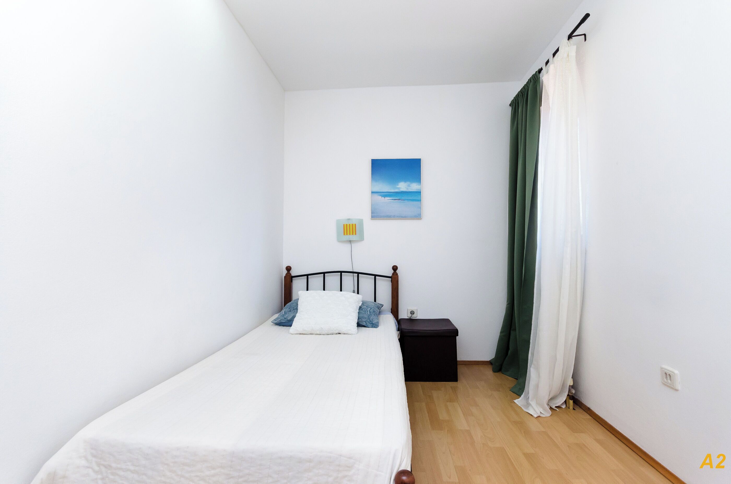 A single-bed room with a wooden headboard, a bedside table, a nightstand, and a wall-mounted light.
