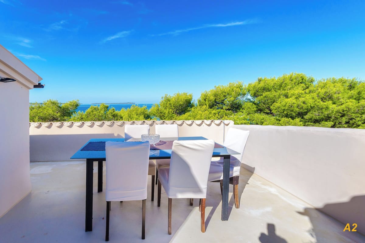 A terrace with a table and chairs, overlooking a scenic view of the sea and greenery.