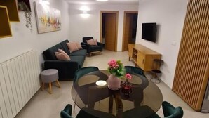 A modern living room with a sofa, a dining table with chairs, a TV, and a ceiling light. - Apartments Cerin (Rovinj)