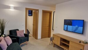 A living room with a dark green sofa, a wooden TV stand, and a television displaying a nature scene. - Apartments Cerin (Rovinj)