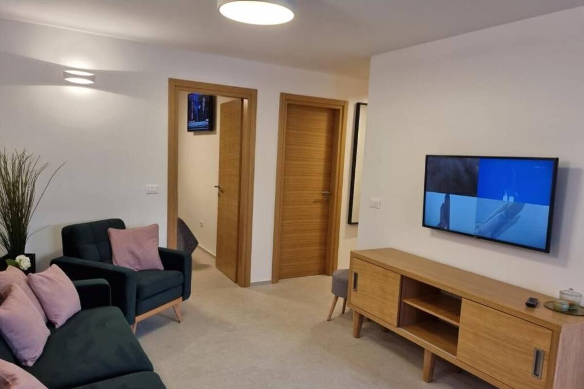 A living room with a dark green sofa, a wooden TV stand, and a television displaying a nature scene.
