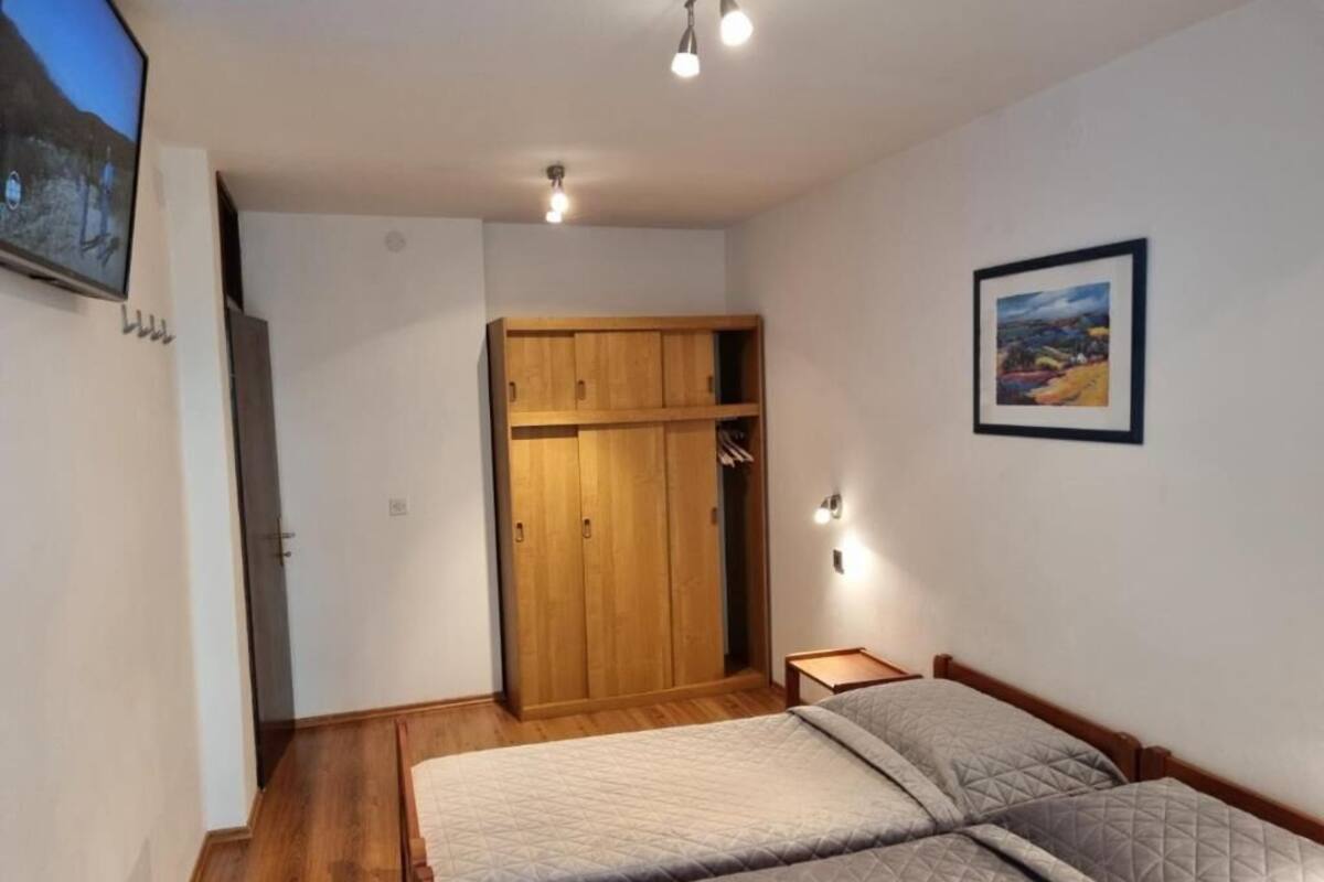 A bedroom with two beds, a wooden wardrobe, a painting on the wall, and a television mounted on the wall.