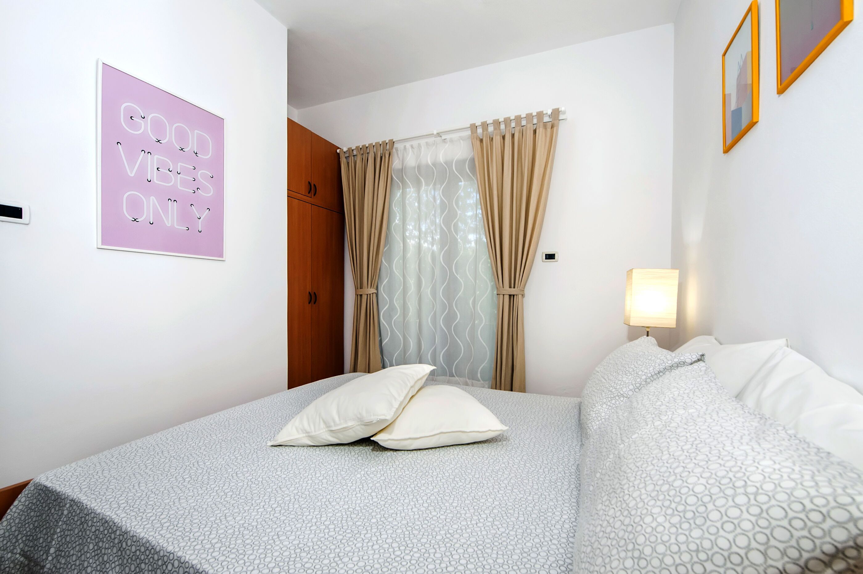 A bedroom with a bed, pillows, a nightstand, a lamp, a window with curtains, a door, and a motivational poster on the wall.