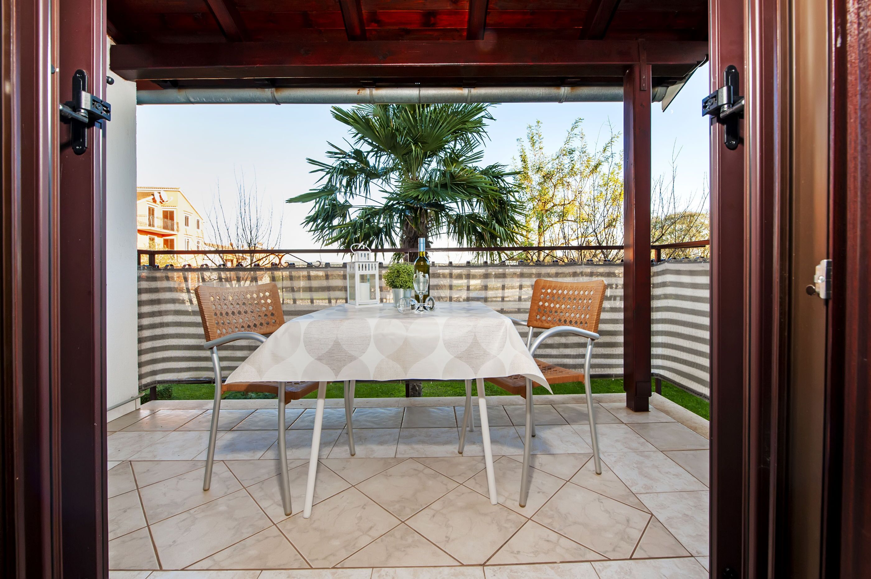 Une terrasse extérieure avec une table et deux chaises, un pot de fleurs et une vue sur des bâtiments et des arbres.