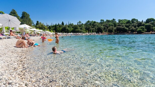 Een kiezelstrand met helder water, parasols en mensen die zonnen.