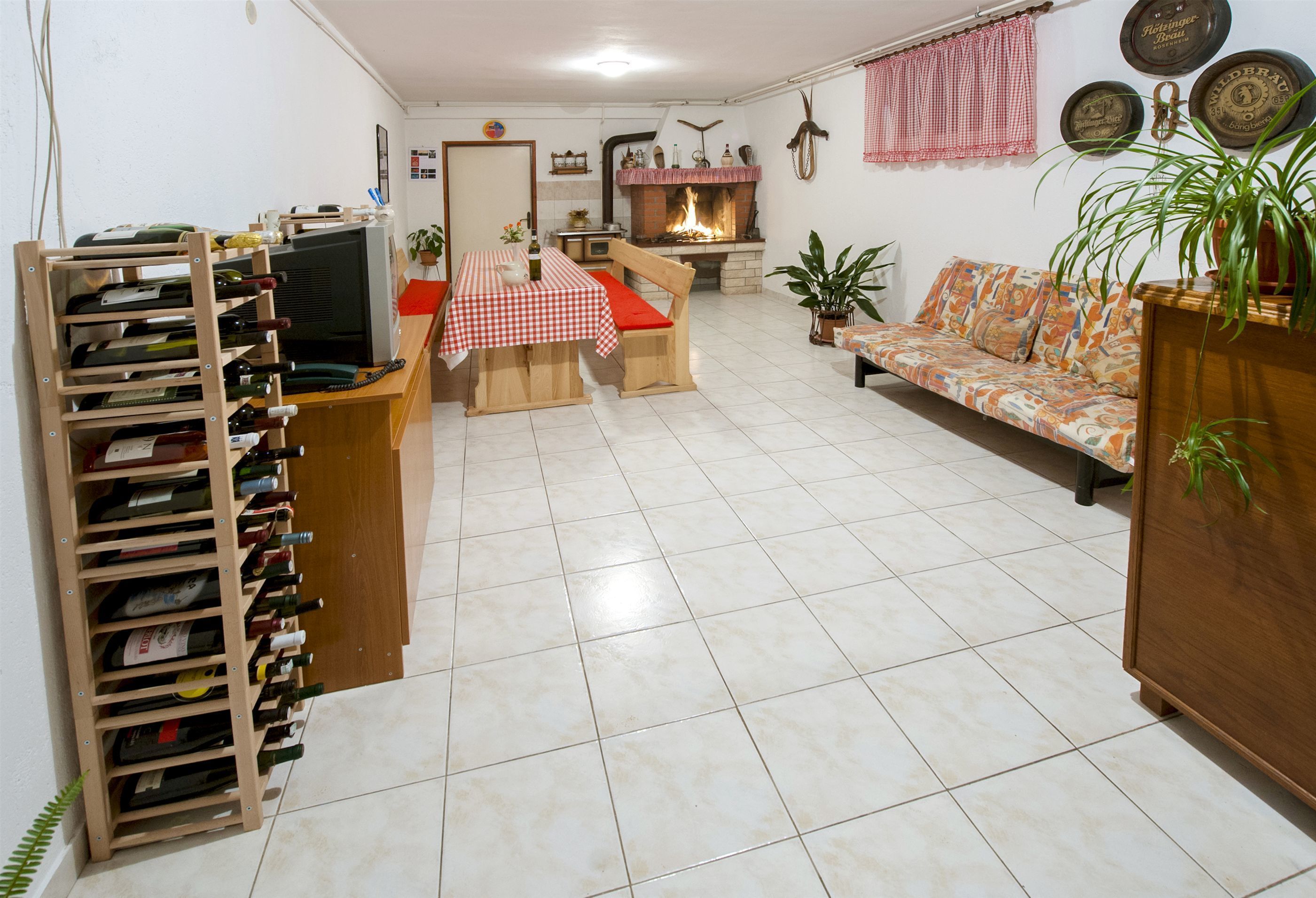 A living room with a fireplace, a sofa, a dining table with a red and white checkered tablecloth, and a wine rack.