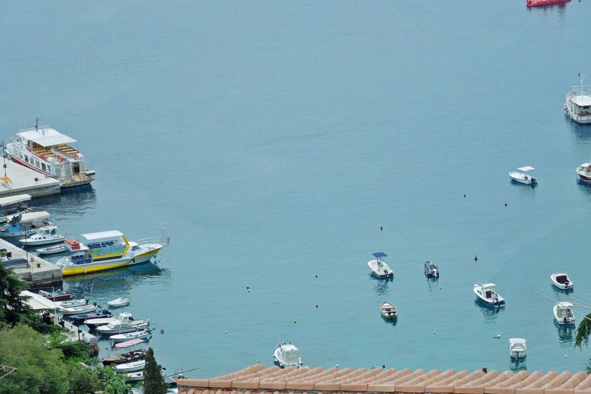 A marina with various boats docked, a red submarine in the water, and a building with a tiled roof in the foreground.