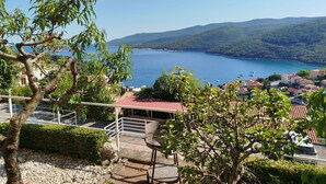 A coastal view with a clear sky, a tree-lined terrace, and a distant view of a bay with boats. - Apartments Elide (Rabac)