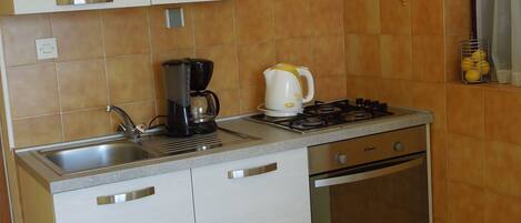 Een compacte keuken met een spoelbak, fornuis en oven, met lichte kasten en een backsplash van oranje tegels.