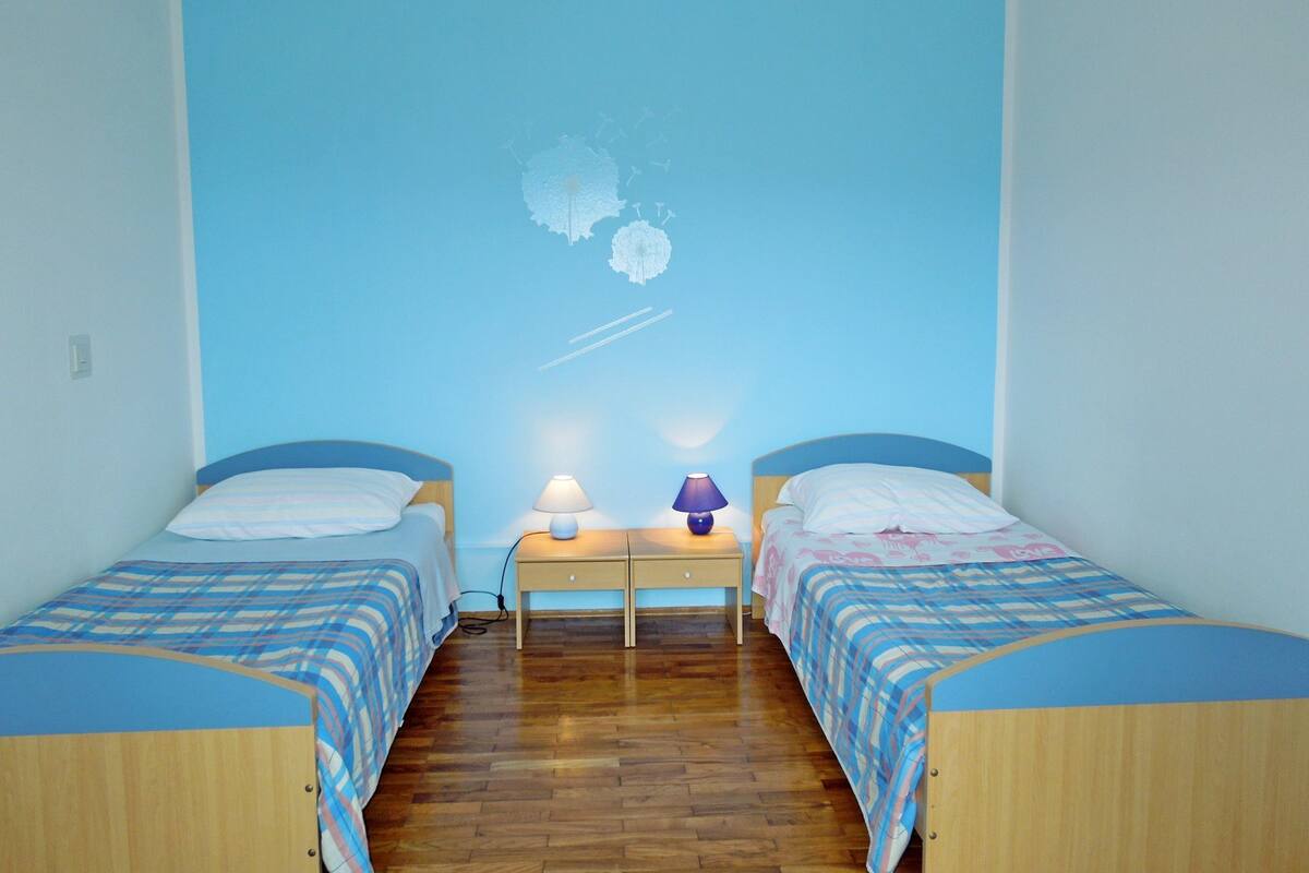 Habitación con dos camas, una mesita de noche y un mural azul claro en la pared.