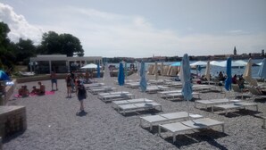 A beach with sun loungers and umbrellas, a building in the background, and a view of the water. - Apartment Loredana (Porec)
