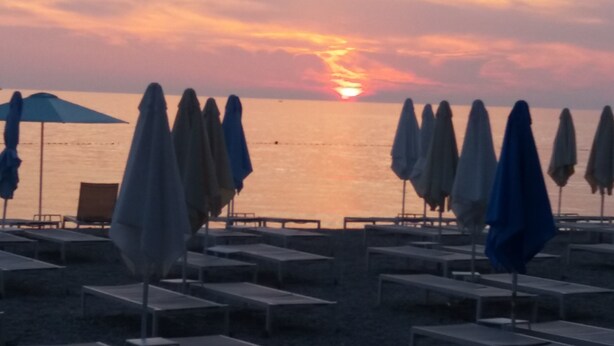 A beach with rows of sun loungers and umbrellas, a sunset in the background, and a calm sea. - Apartment Loredana (Porec)