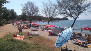 A beach scene with people sunbathing, swimming, and walking along the shore. - Apartment Loredana (Porec)