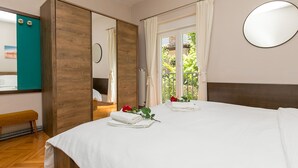 A bedroom with a wooden wardrobe, a bed with white linens, a round mirror, and a view of greenery through the window. - Apartment Loredana (Porec)