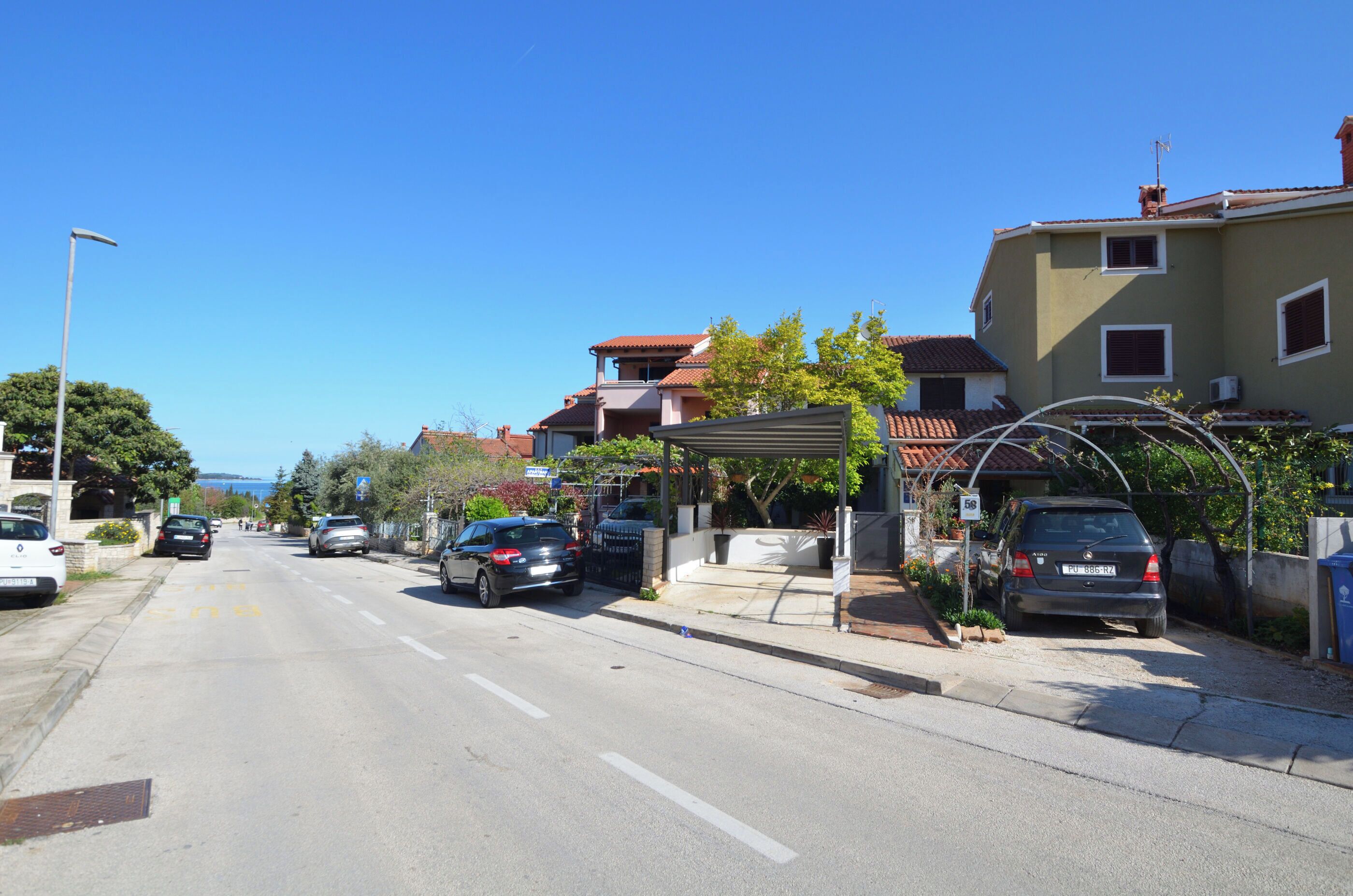 A street with parked cars, a covered parking area, and residential buildings.