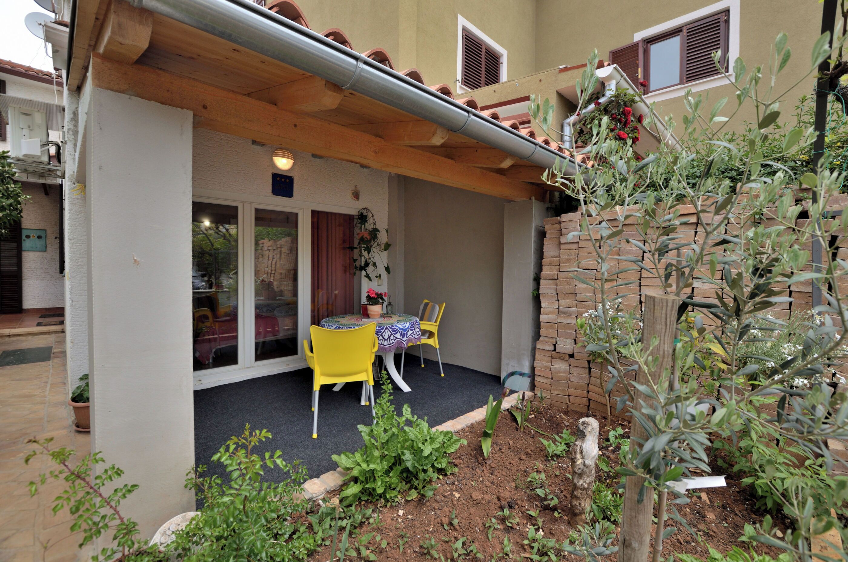 A covered patio with a table and chairs, a brick wall, and potted plants.