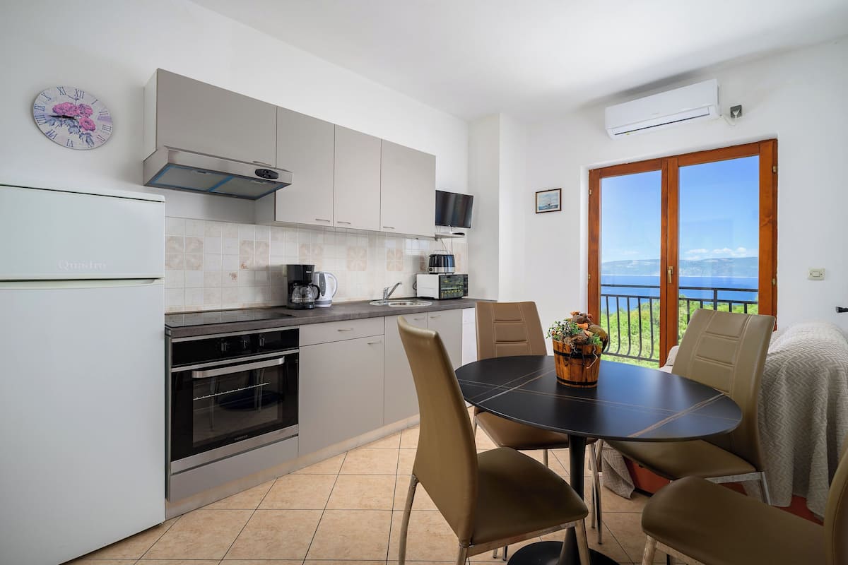 A modern kitchen with a dining area, a TV, and a view of the sea.