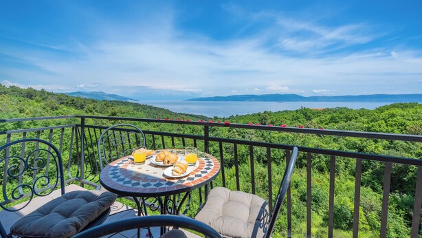 A balcony with a table set for breakfast, overlooking a lush green landscape and a body of water. - Apartments Wellness (Ravni)