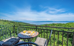 A balcony with a table set for breakfast, overlooking a lush green landscape and a body of water. - Apartments Wellness (Ravni)
