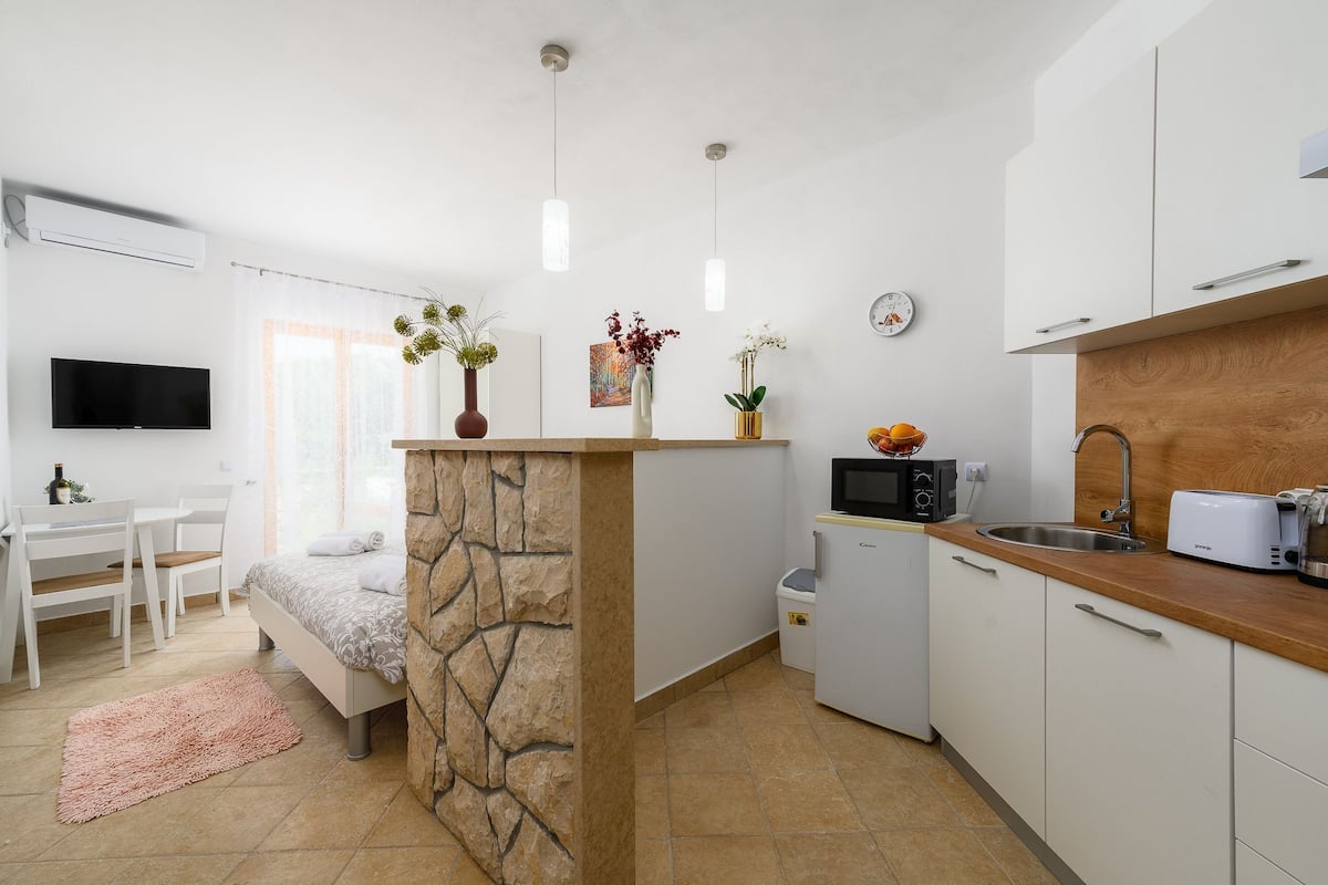 A compact hotel room with a kitchenette, a dining area, and a TV.