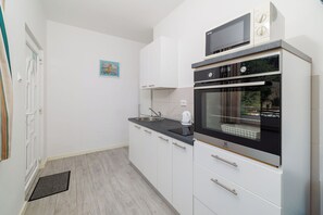 Een kleine keuken met witte kastjes, een inbouwoven en een magnetron.