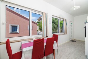Een eetruimte met een tafel en stoelen, grote ramen en uitzicht op een gebouw.