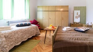 Een slaapkamer met twee bedden, een houten garderobe, een klein tafeltje met handdoeken en een raam met groene gordijnen.