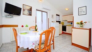 Een eethoek met een tafel gedekt voor twee personen, een aan de muur bevestigde televisie en een keuken op de achtergrond.