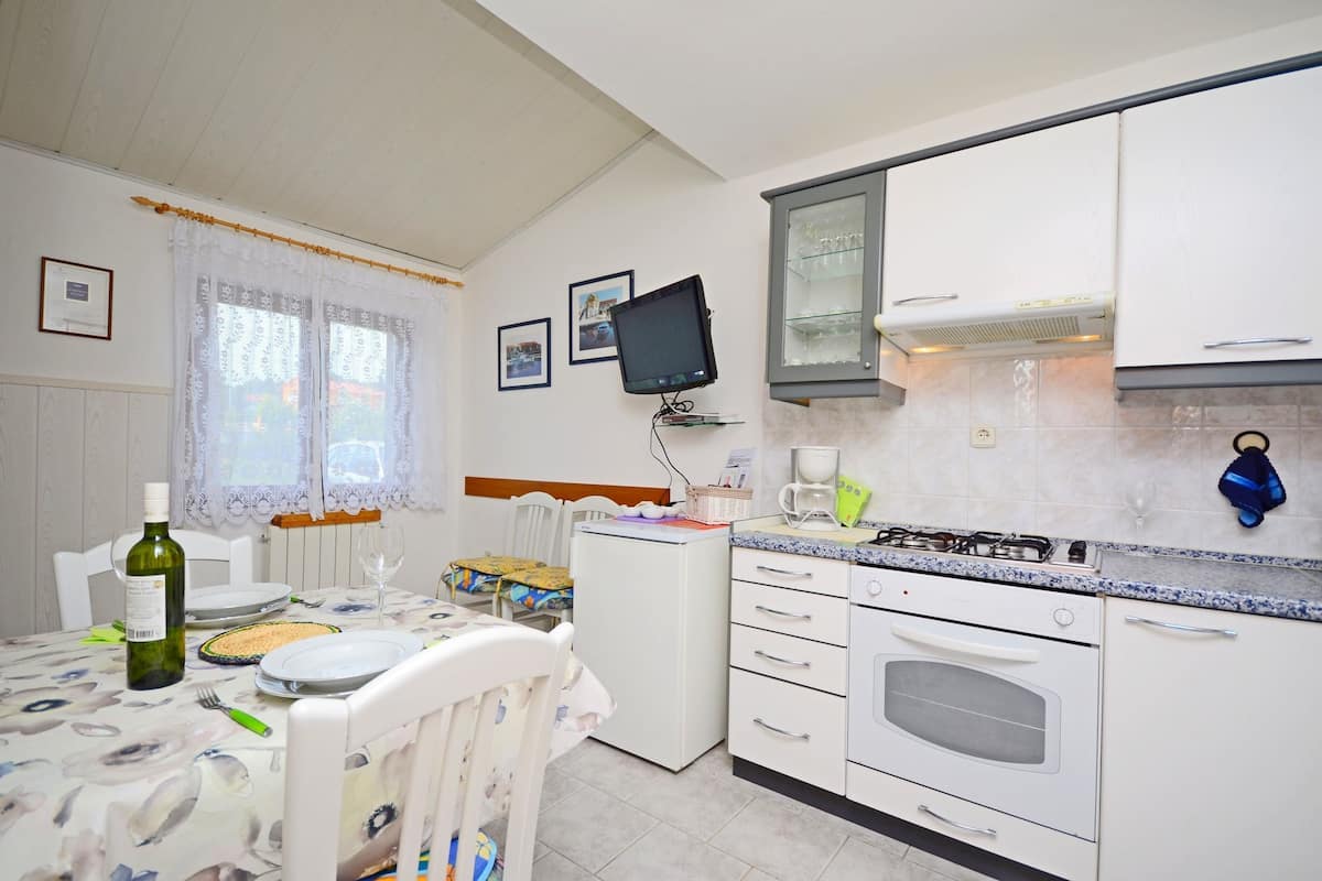 A compact kitchen with a dining area, a small refrigerator, a stove, and a television mounted on the wall.