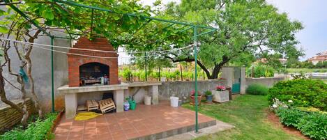 A brick outdoor kitchen with a grill, surrounded by a garden with various plants and a pergola.