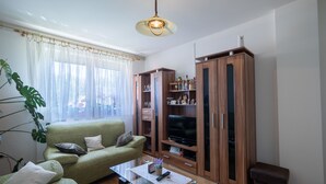 A living room with a green sofa, a glass coffee table, wooden cabinets, and a large window with sheer curtains. - House Marijana (Smoljanac)