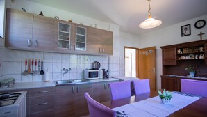 A modern kitchen with wooden cabinets, a microwave, and a dining table with purple chairs. - House Marijana (Smoljanac)