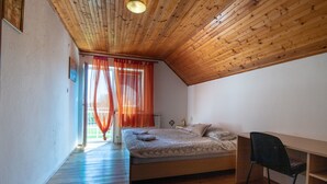 A bedroom with a wooden ceiling, a bed, a chair, and a window with orange curtains. - House Marijana (Smoljanac)