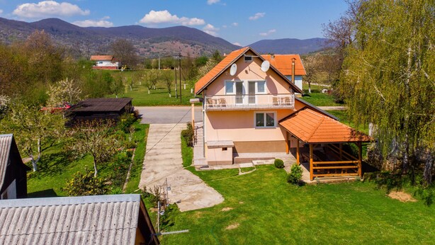 A two-story house with a balcony, a garden, and a view of mountains in the background. - House Marijana (Smoljanac)