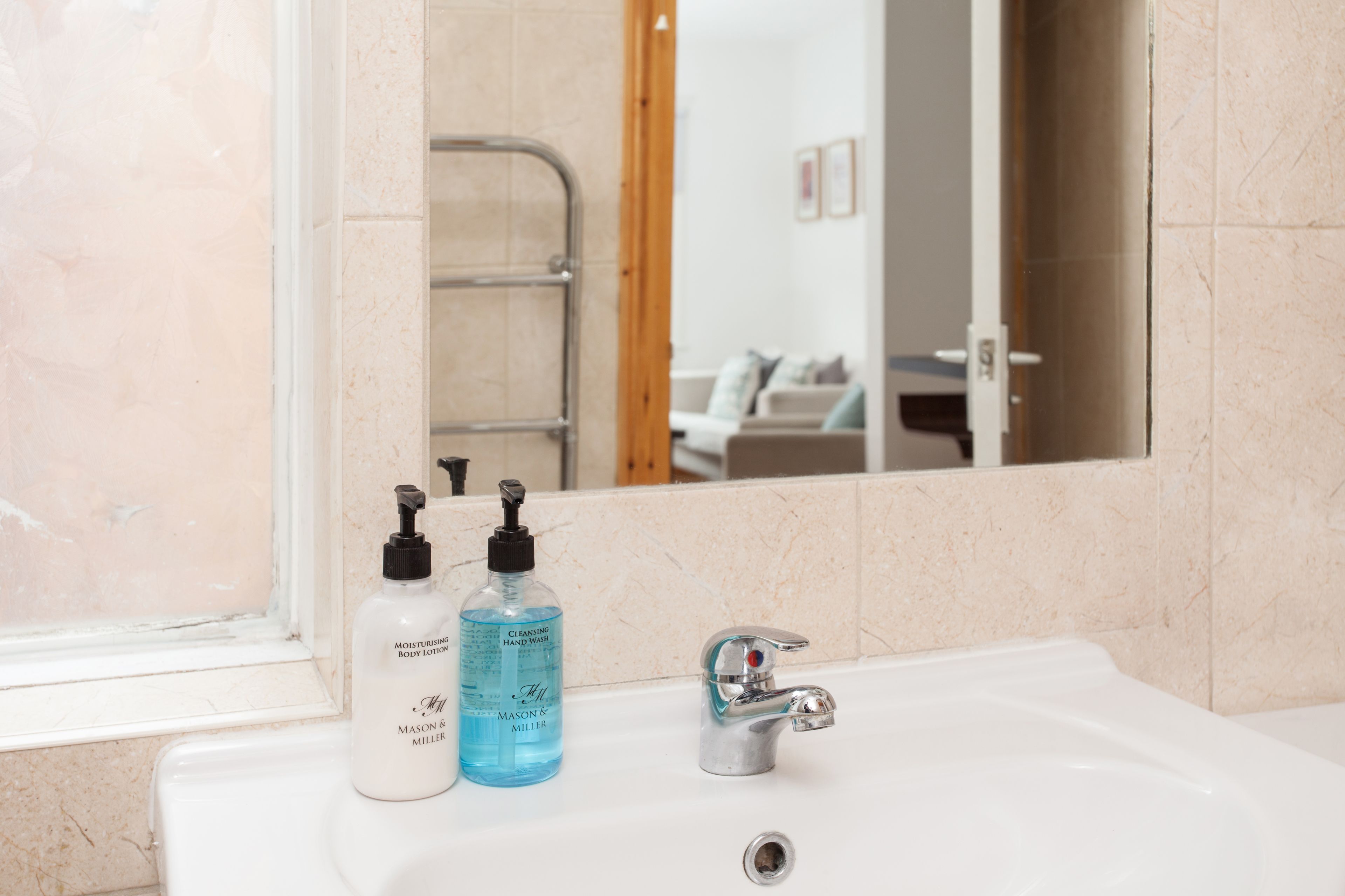 A bathroom with a sink, two bottles of body lotion, and a mirror reflecting a shower area.