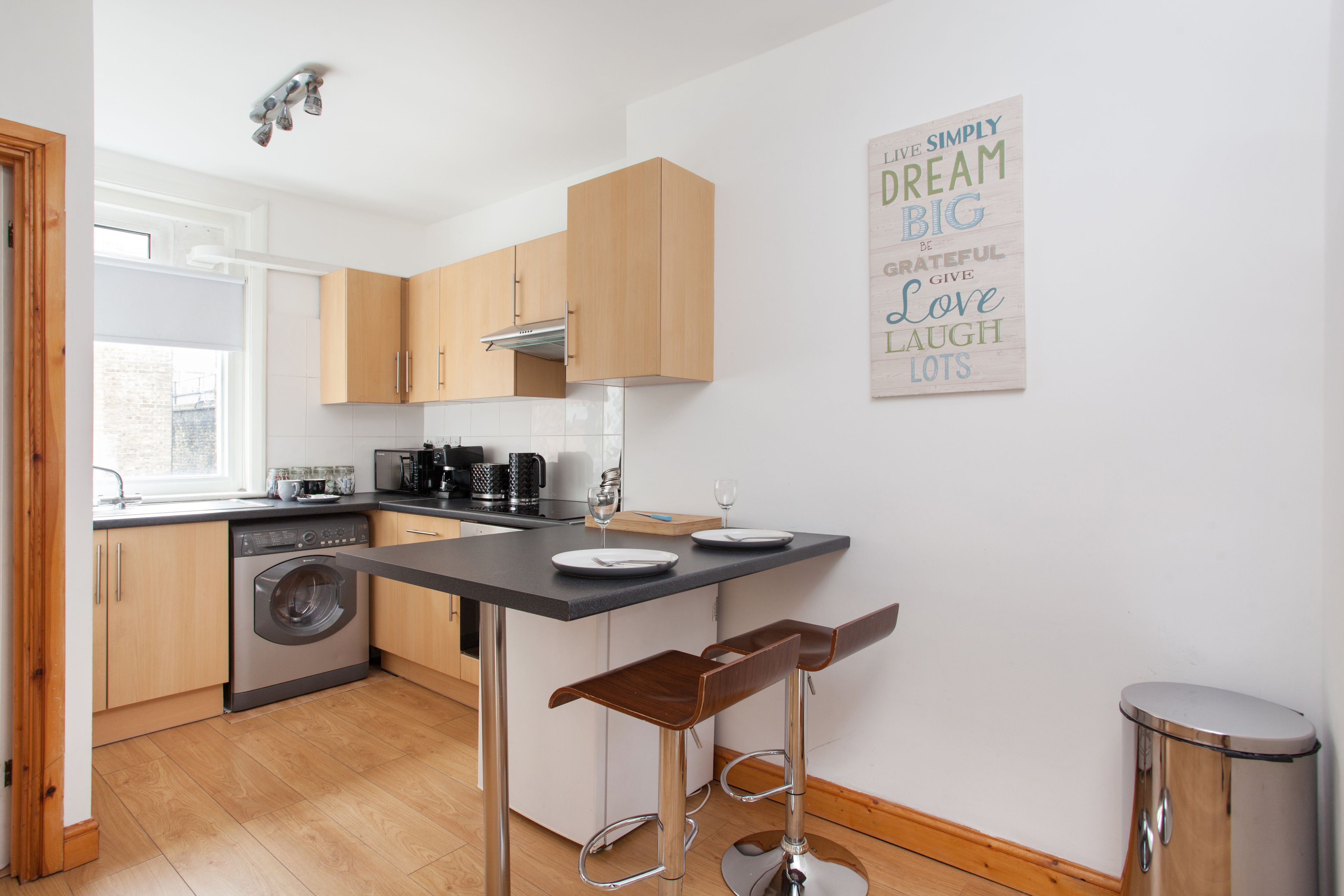 Une cuisine moderne avec des meubles en bois, un lave-linge encastré et un coin bar avec des tabourets.