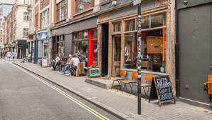A street with outdoor seating at a café, a signboard, and a building with a red door. - Basic Apartment for Two Amazing Location (London)