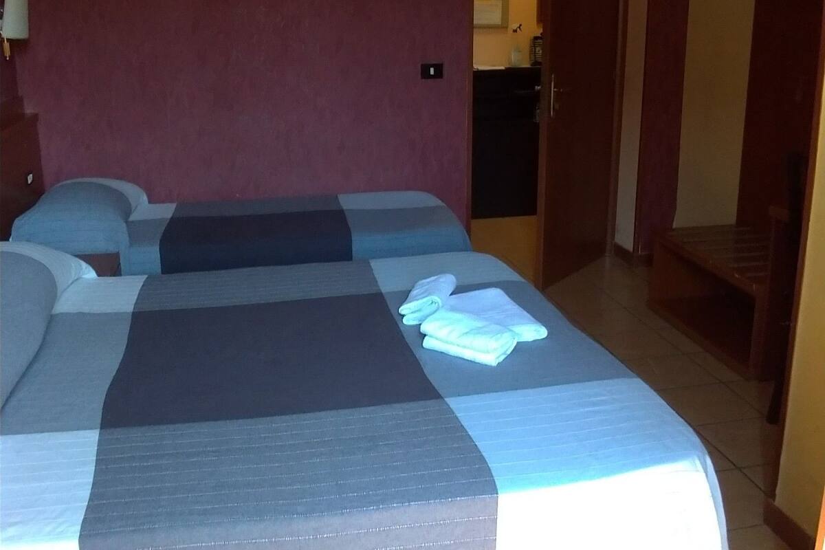 Quarto de hotel com uma cama grande, um ventilador de teto, um aparelho de ar condicionado e uma televisão na parede.