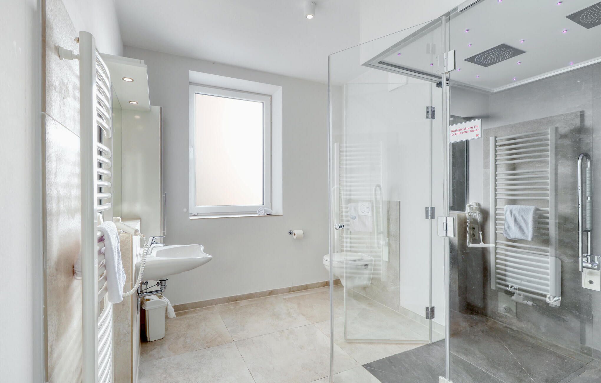 Een moderne badkamer met een glazen douchecabine, een wastafel met spiegel en een raam voor natuurlijk licht.