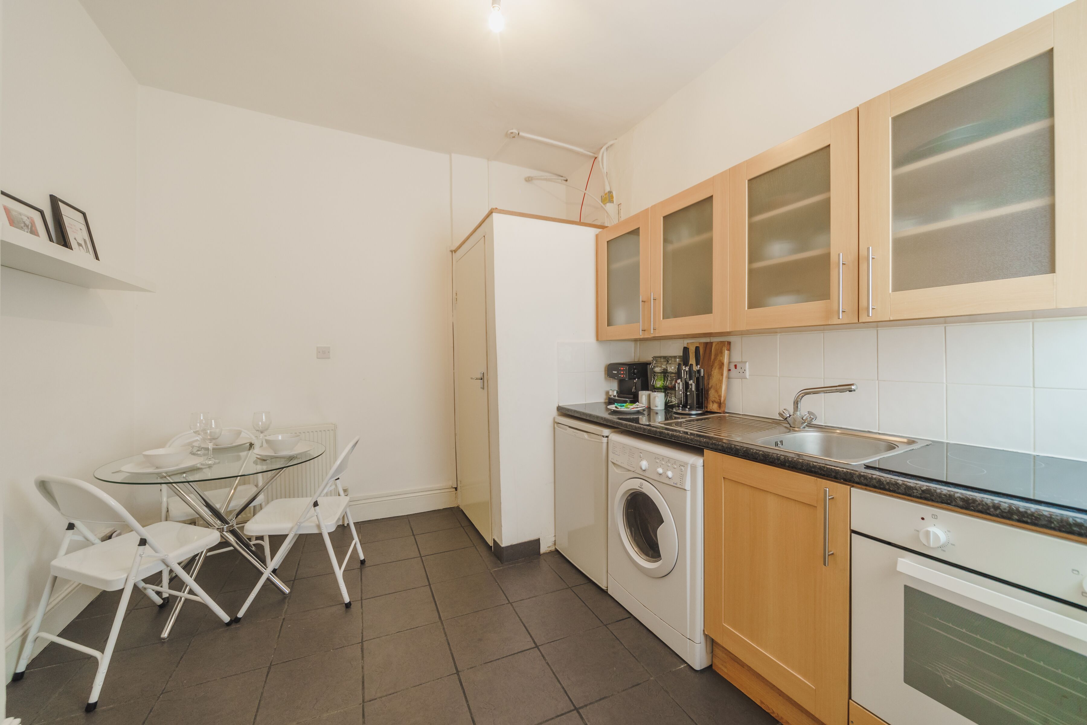 A compact kitchen with a washing machine, a sink, and a dining area with a glass table and chairs.