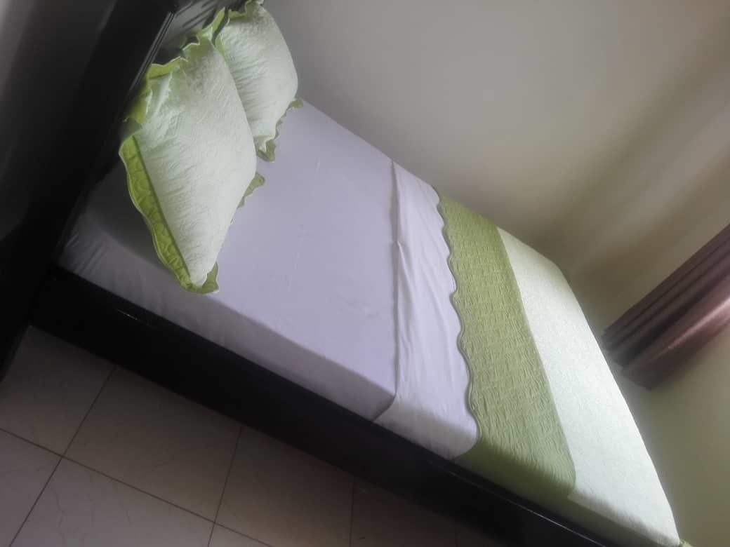 A single bed with a white mattress and green pillows, a black frame, and a tiled floor.