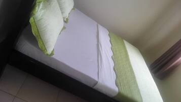 A single bed with a white mattress and green pillows, a black frame, and a tiled floor.